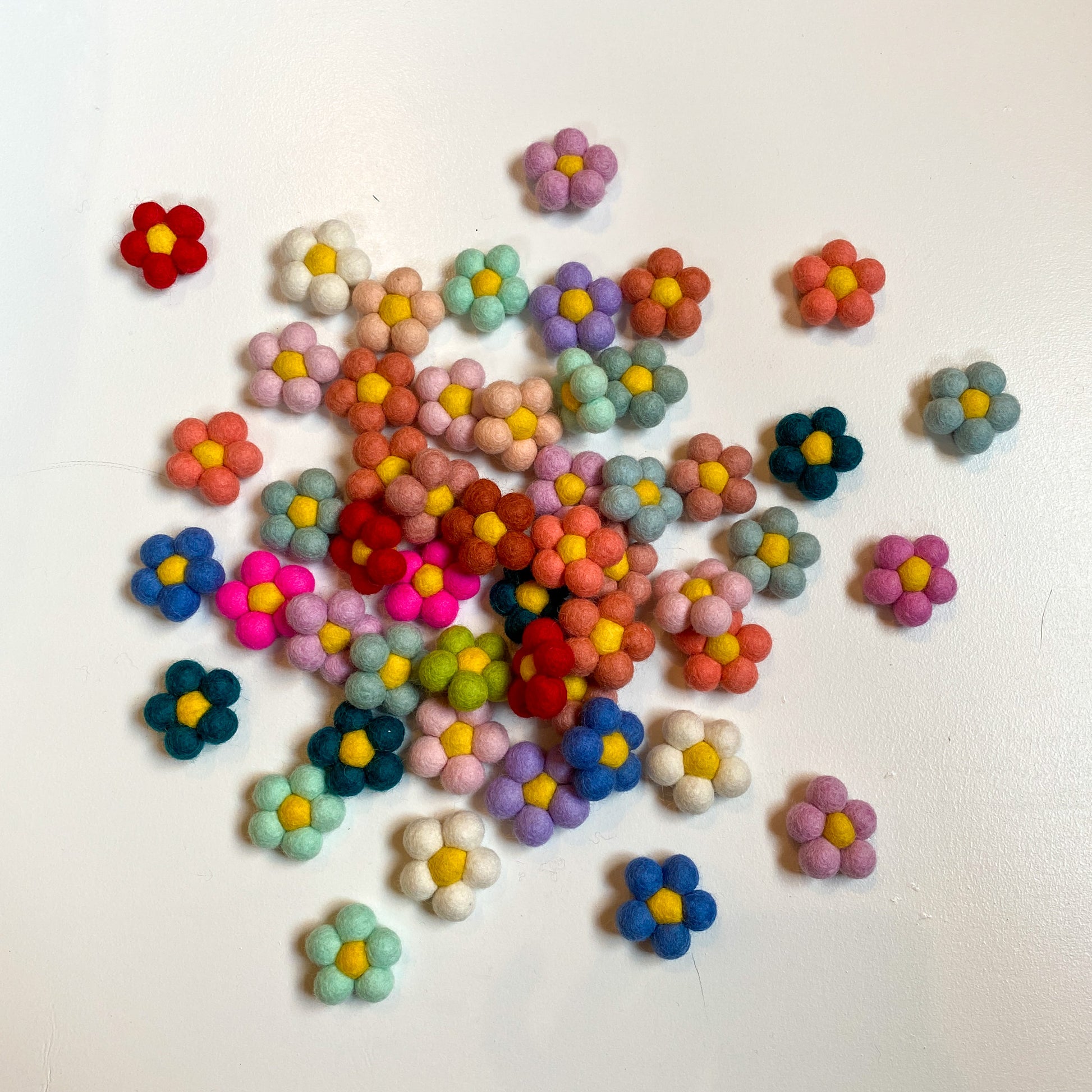 A slightly scattered pile of felt flowers in a variety of colors.